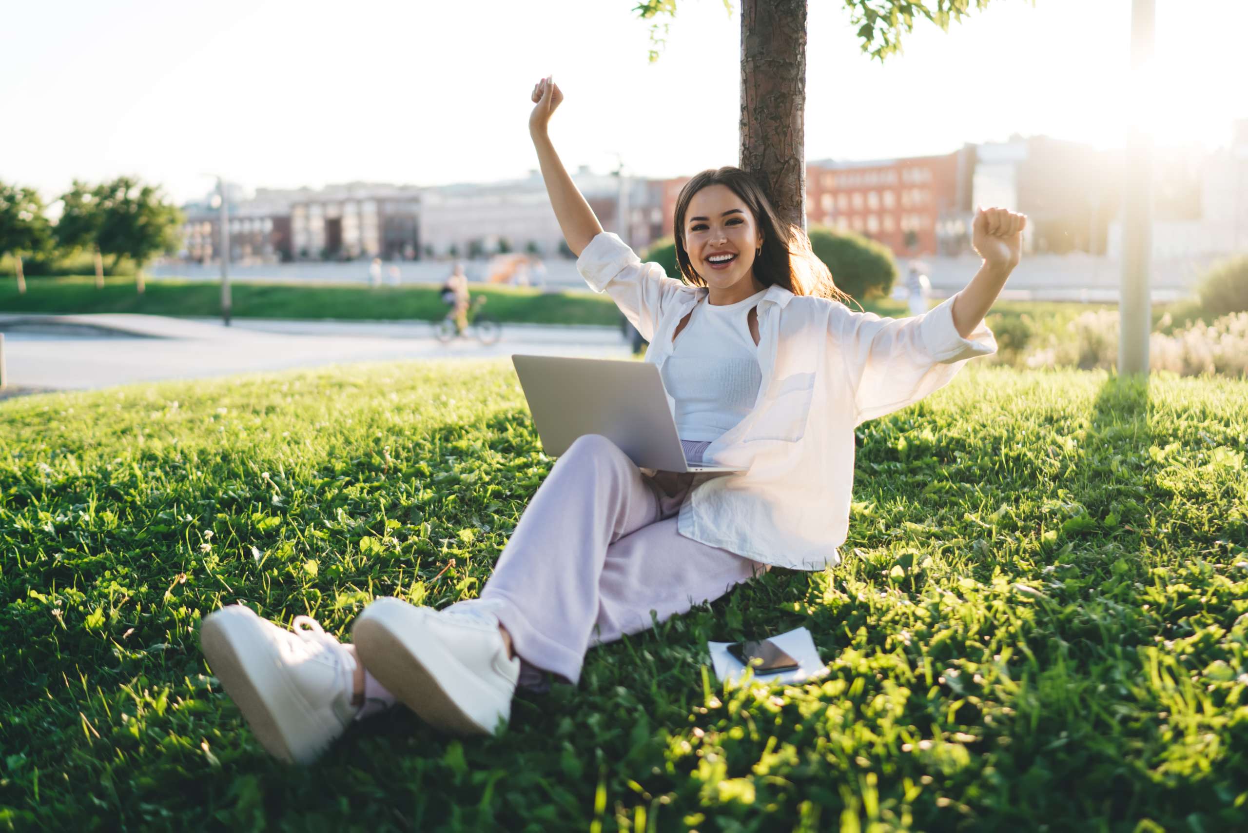 Thrilled happy woman sitting near tree celebrating victory in park